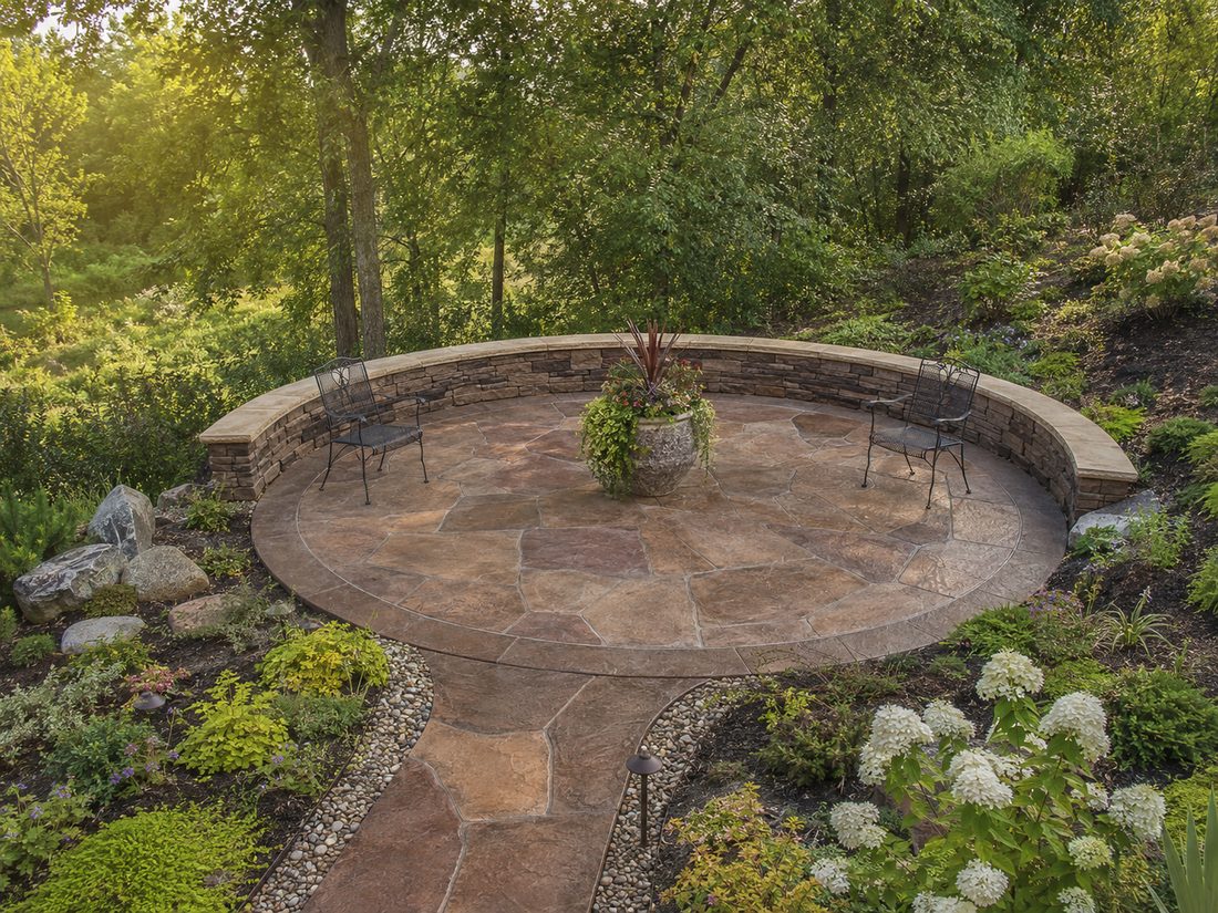 Circular stamped concrete patio with stone seat wall in a wooded Sioux Falls, SD backyard
